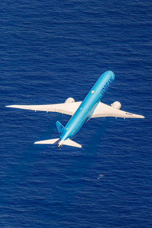 An aerial view of a blue and white commercial airplane flying over the ocean.