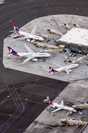 An aerial view of an airport tarmac with several commercial airplanes parked at the gates, connected to the terminal building.