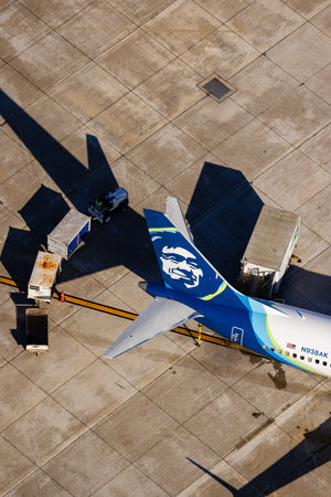 An aerial view of an airport tarmac with a large blue and white airplane parked on the runway, surrounded by various ground support vehicles and equipment.