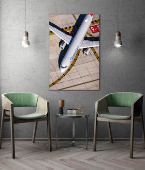 a large airplane painted in white and blue colors, with a red and white logo on its tail, displayed on a wall above two green chairs and a small table.