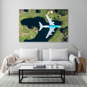 a large, white airplane flying over a golf course with a pond below.
