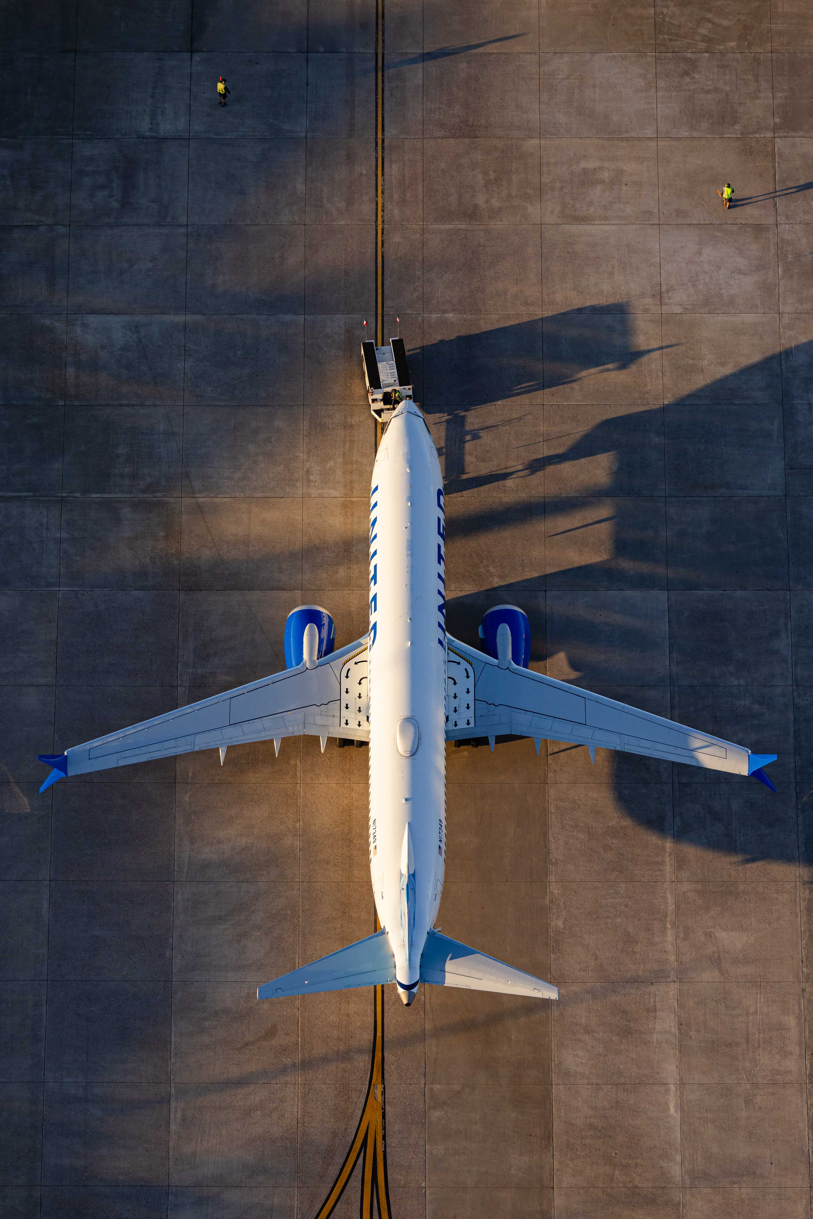An aerial view of a large commercial airplane on a runway, with a person visible on the ground near the airplane.