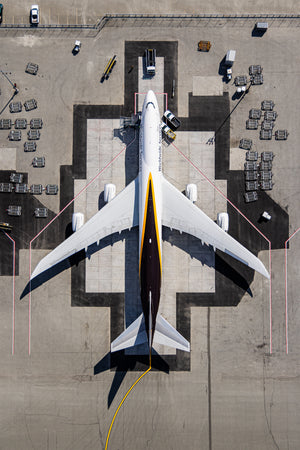 An aerial view of a large white airplane with a yellow stripe on its tail, parked on a tarmac at an airport.