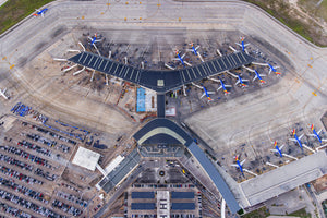 An aerial view of an airport with multiple airplanes parked at the terminal and a parking lot filled with cars.