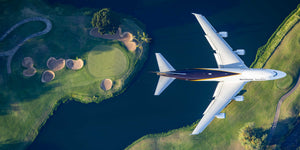 An aerial view of a large commercial airplane flying over a golf course with a body of water below.