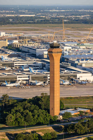 an aerial view of an airport with a tall orange tower in the center, surrounded by various buildings and vehicles.