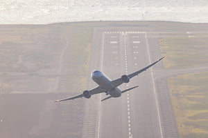 An airplane is flying low over a runway, with the ocean visible in the background.