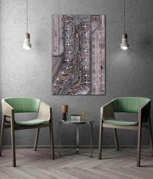 a modern and minimalist interior design with a large wall-mounted painting depicting an airport terminal with multiple airplanes. Two green chairs are positioned in front of the painting, creating a cozy seating area. The room has a neutral color palette with gray walls and a wooden floor, and the overall design appears to be contemporary and visually appealing.