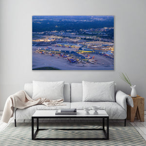 a large aerial view of an airport at night, with numerous airplanes and airport buildings illuminated against the dark sky.