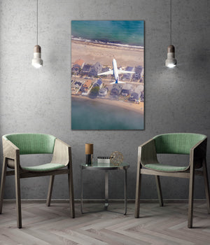 a large aerial photograph of a beach and houses, with a plane flying over the scene. The photograph is displayed on a wall, and there are two green chairs positioned in front of it.