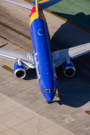 An aerial view of a large commercial airplane on the tarmac, with its landing gear down and the wings extended.