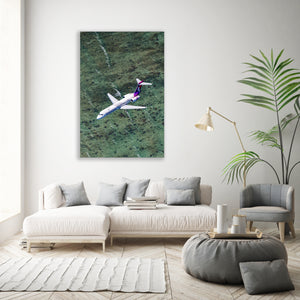a large airplane flying over a grassy field, with a white sofa and a potted plant in the foreground.