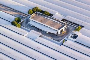 An aerial view of a large white building with a curved roof, surrounded by trees and other structures.