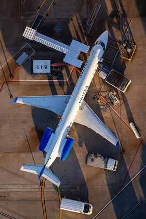 An aerial view of an airplane parked at an airport, with various ground support equipment and vehicles nearby.
