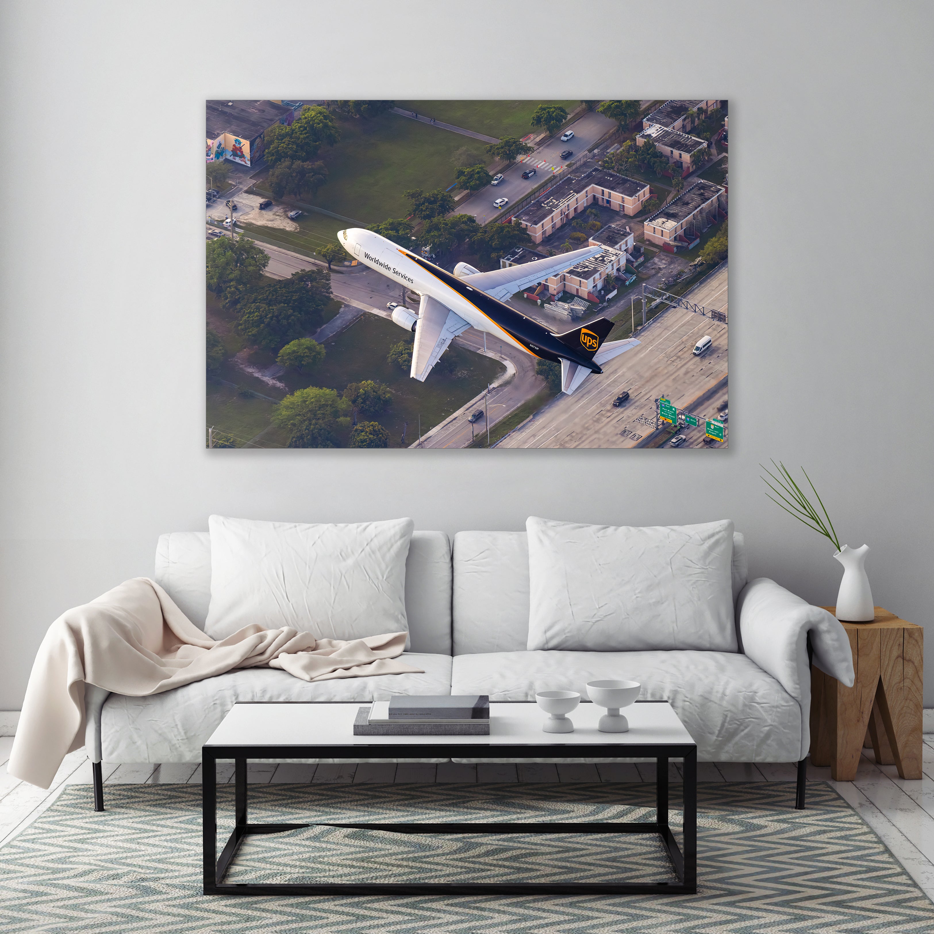 a large aerial view of a white airplane flying over a cityscape with buildings, trees, and roads.