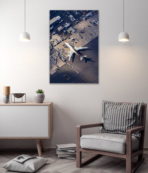 a large airplane flying over a city, with a building and parking lot visible below.