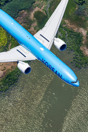 An aerial view of a large commercial airplane flying over a body of water, with the word "KOREAN" visible on the side of the aircraft.