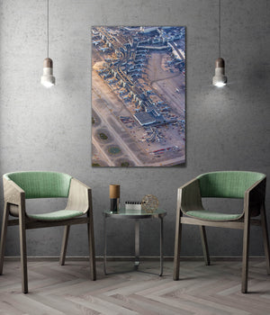 a modern living room with a large wall-mounted painting depicting an aerial view of an airport terminal. The room is furnished with two green chairs, and a small table is placed between them. The overall design and decor create a contemporary and stylish atmosphere.