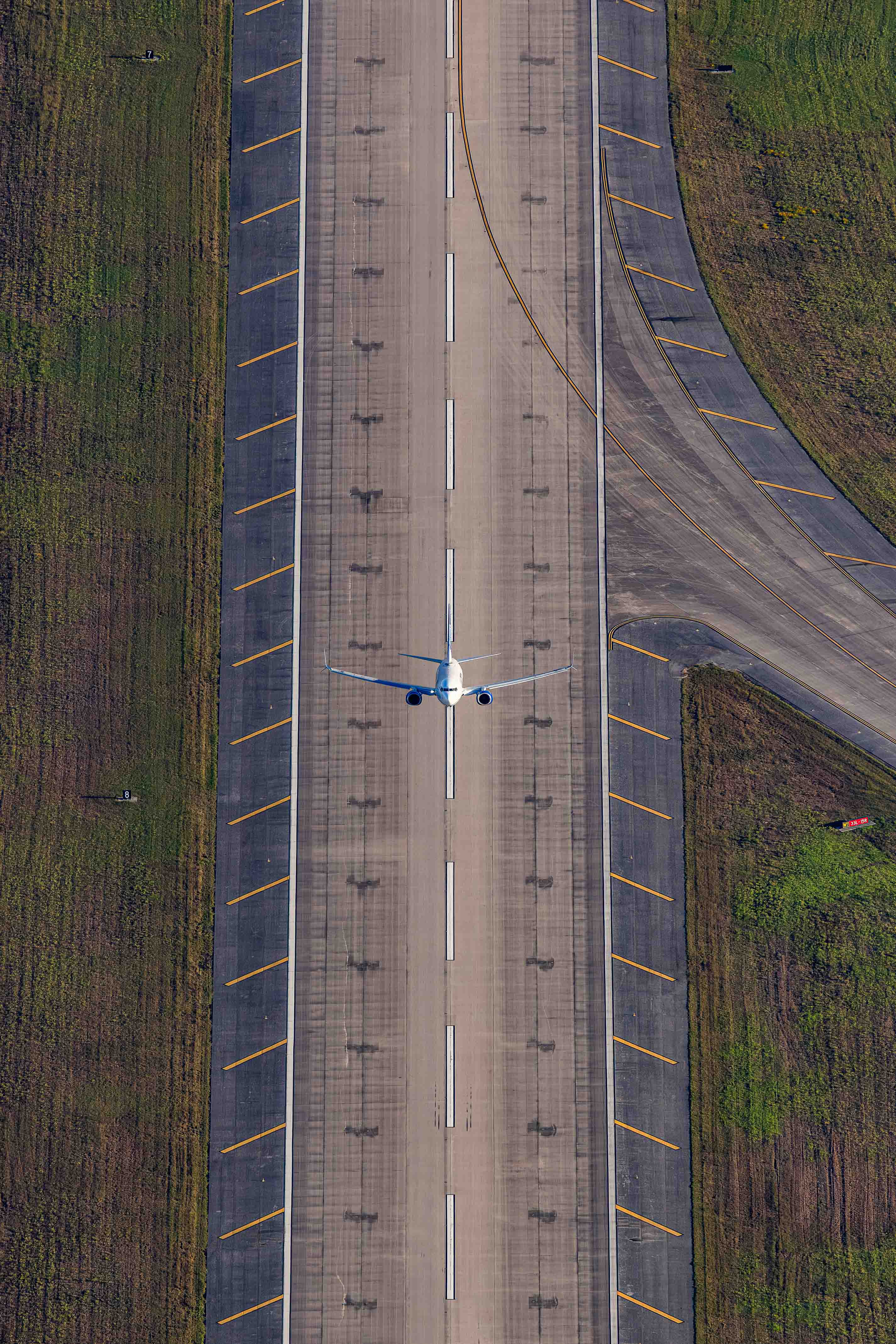 An aerial view of a runway with a white airplane on the tarmac.