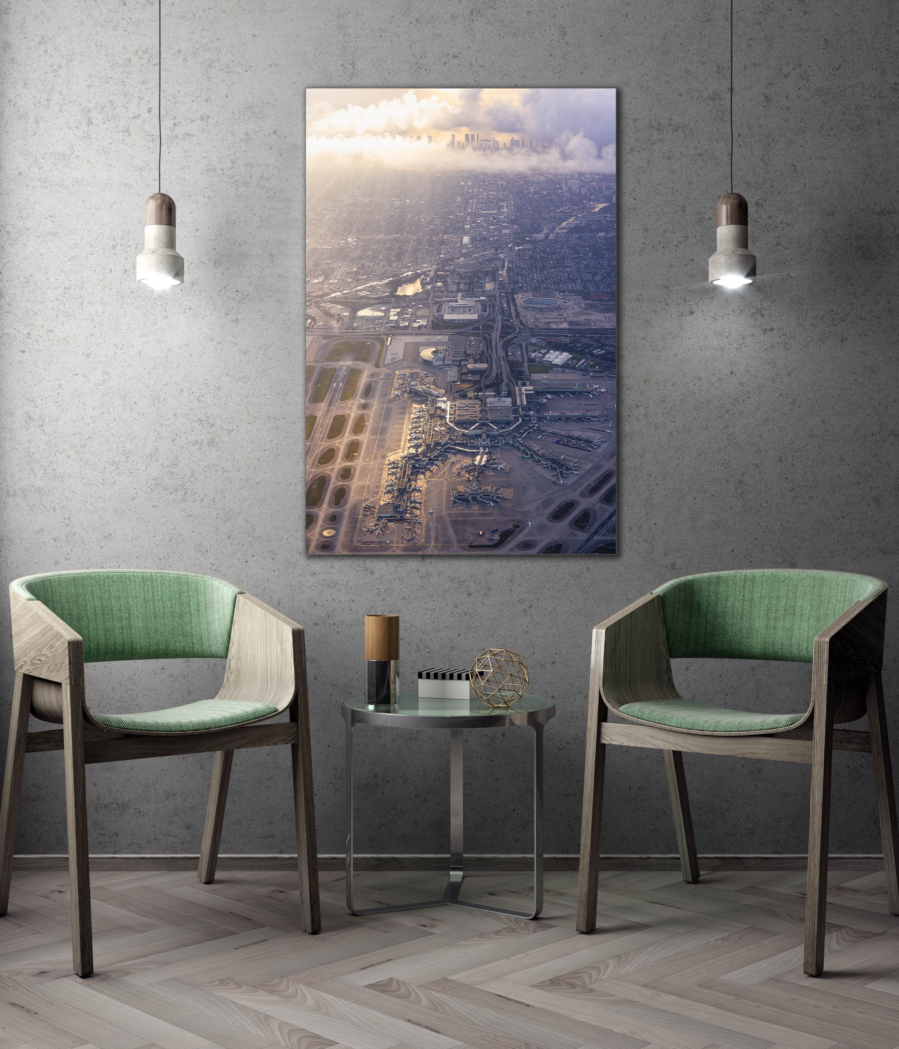 a modern living room with a large framed aerial view of a cityscape hanging on the wall. The room is furnished with two green chairs and a small round table, creating a cozy and inviting atmosphere.