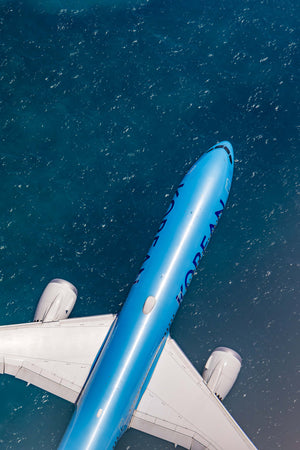 An aerial view of a large commercial airplane flying over a body of water, with the ocean visible below.