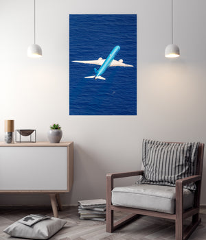a modern living room with a minimalist design. The focal point is a large poster of a blue airplane flying over a body of water, creating a sense of movement and adventure. The room is furnished with a wooden chair, a white cabinet, and a stack of books, creating a cozy and inviting atmosphere.