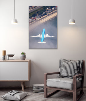 a large blue airplane flying over a coastal city, with a white wall and a wooden chair in the foreground.