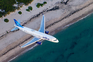 An aerial view of a JetBlue airplane flying over a beach and ocean.