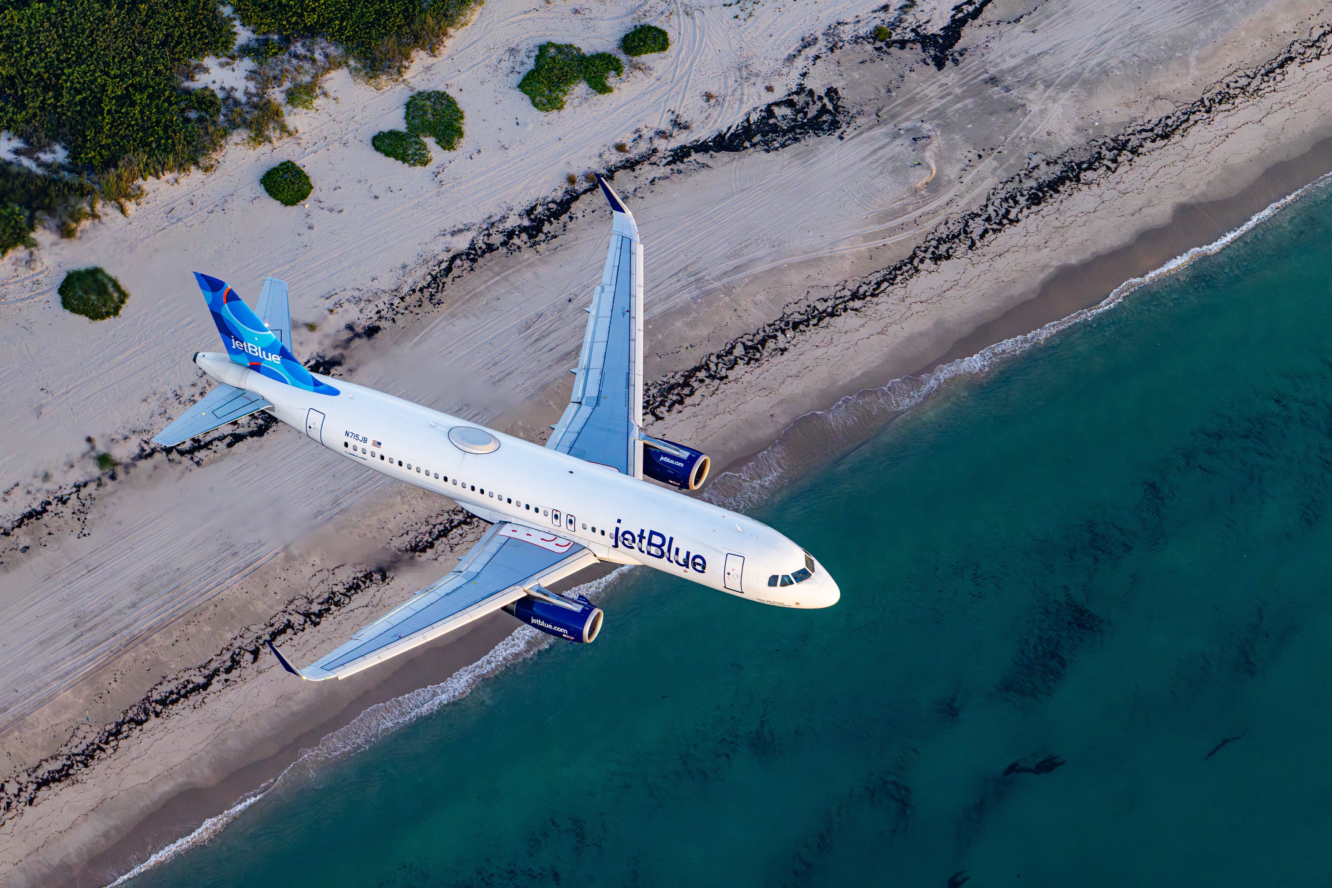 An aerial view of a JetBlue airplane flying over a beach and ocean.