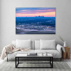 a large, high-resolution photograph of a city skyline at sunset, hanging on a wall above a white sofa and a coffee table in a living room setting.