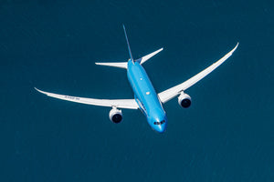 An aerial view of a large blue commercial airplane flying over a body of water.