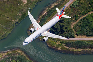 An American Airlines passenger jet is flying over a river, with the surrounding landscape visible below.