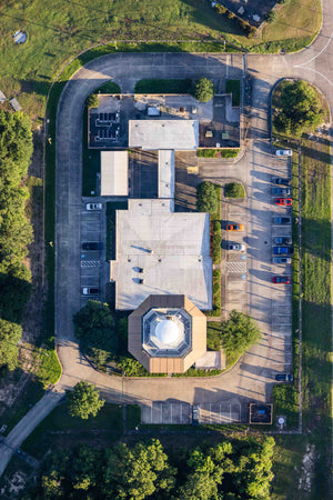 An aerial view of a large building with a dome-shaped roof, surrounded by a parking lot with several cars parked in it.