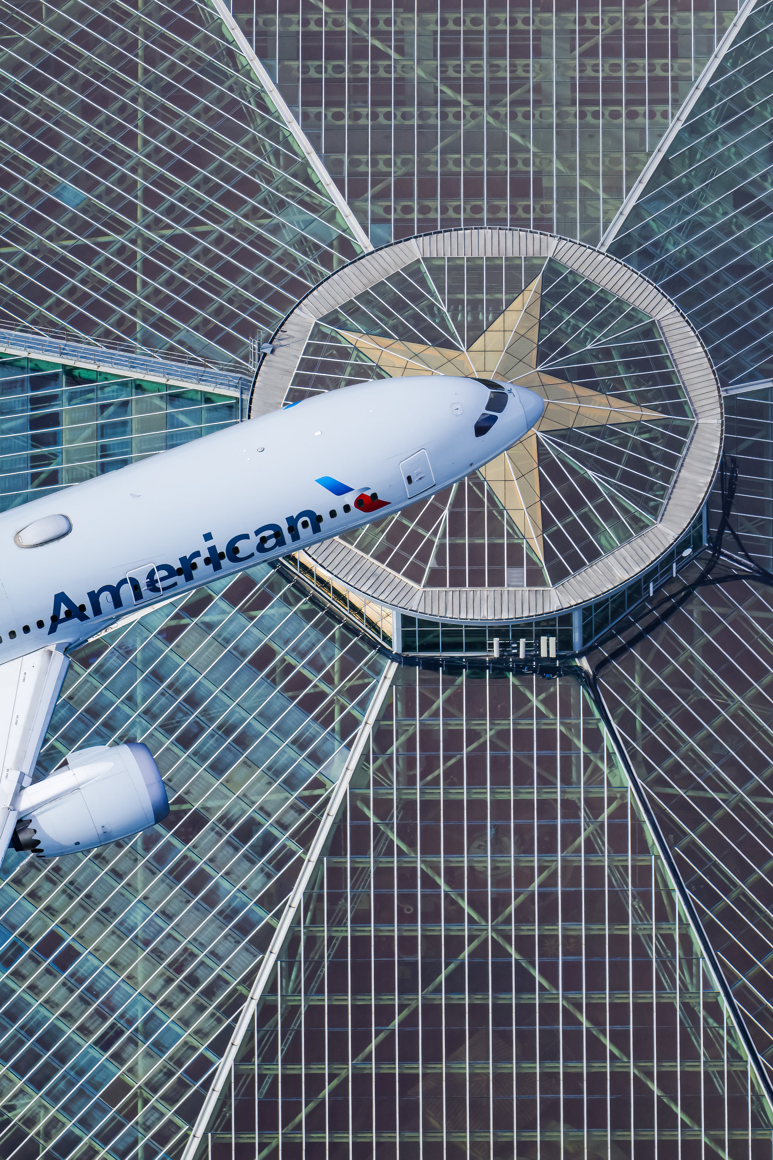 An American Airlines passenger jet is flying over a modern glass and steel building with a distinctive star-shaped design.