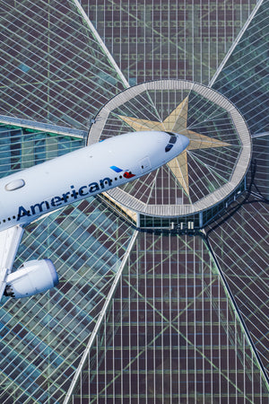 An American Airlines passenger jet is flying over a modern glass and steel building with a distinctive star-shaped design.