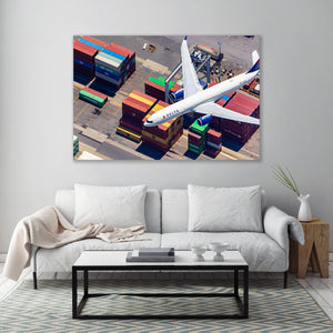 a large airplane flying over a busy airport with cargo containers below it.