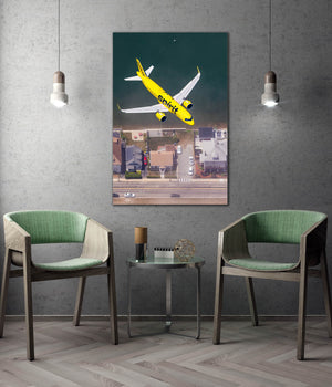 a large framed picture of a yellow airplane flying over a cityscape, with two green chairs positioned in front of it.