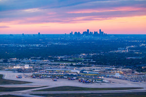 An aerial view of a bustling city skyline at dusk, with the airport in the foreground and the city's skyscrapers visible in the distance.