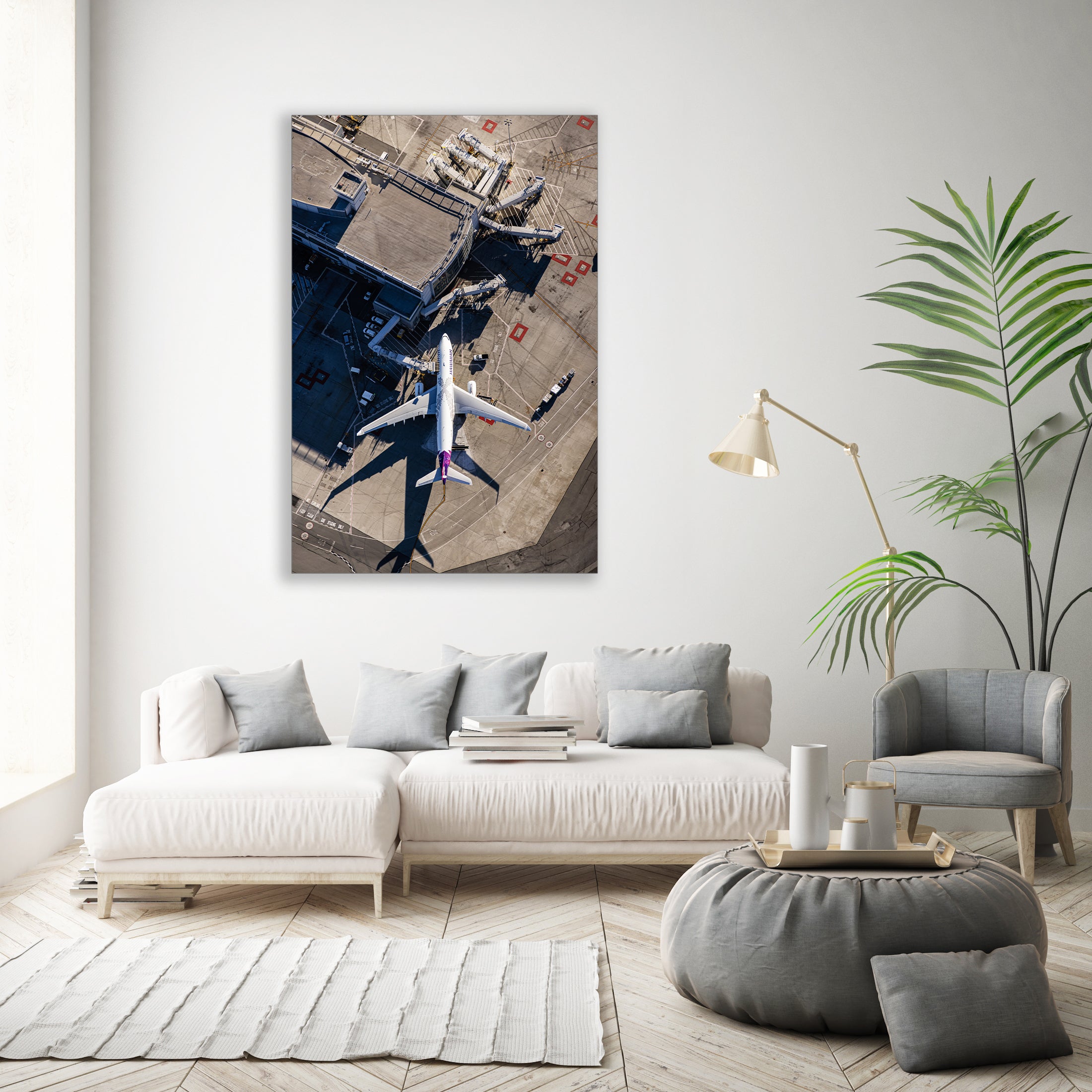 a large white sofa, a coffee table, a potted plant, and a framed aerial photograph of an airport tarmac with airplanes.