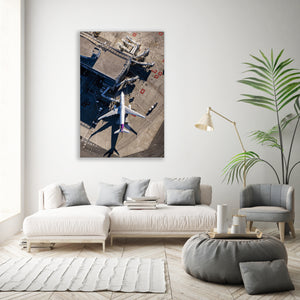 a large white sofa, a coffee table, a potted plant, and a framed aerial photograph of an airport tarmac with airplanes.
