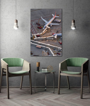 a large aerial view of an airport tarmac with airplanes and airport vehicles, as well as a small table with two green chairs in the foreground.