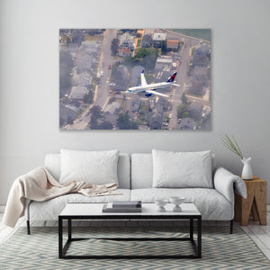 an aerial view of a white sofa and a coffee table in a living room, with a large framed picture of an airplane flying over a residential area hanging on the wall above the sofa.