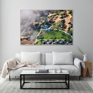 a large aerial view of a landscape with a blue airplane flying over a grassy area, with a small town visible below.