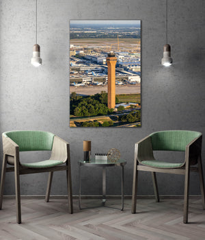 a modern living room with a large wall-mounted painting depicting an aerial view of an airport and its surrounding landscape. The painting is hung above a coffee table with two green chairs placed in front of it.