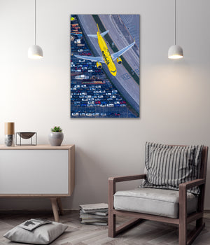 a large yellow airplane flying over a busy highway filled with cars, creating a striking visual contrast between the natural and man-made elements.