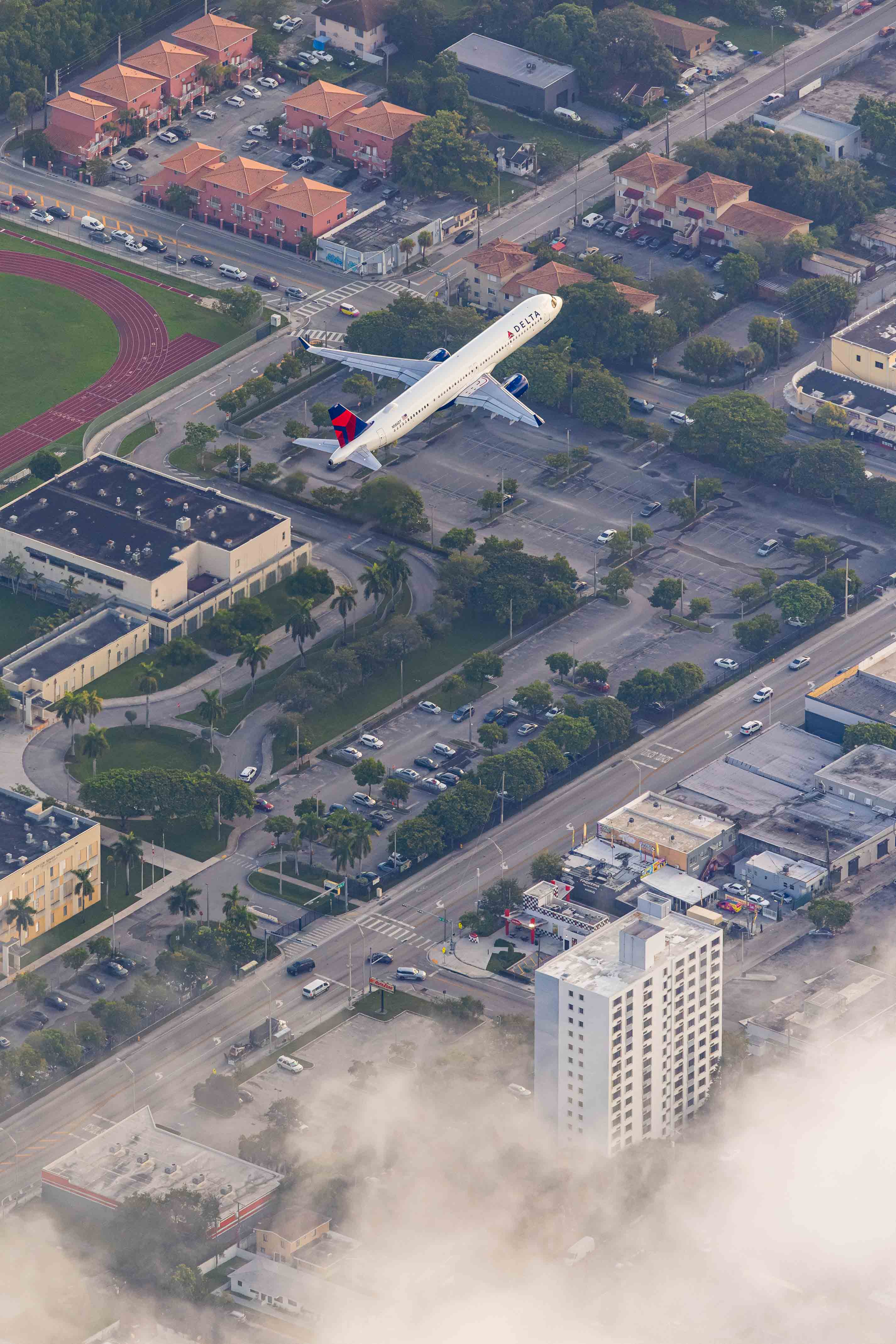 An aerial view of a city with a large airplane flying over it, surrounded by buildings, roads, and other urban elements.