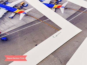 The image is a close-up of a printed photograph featuring a model airplane on an airport tarmac, with a signature in the corner.