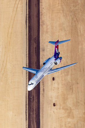 An aerial view of a Hawaiian Airlines passenger jet flying over a runway.