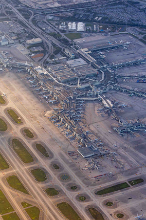 An aerial view of an airport complex with multiple runways, terminals, and aircraft parked or moving.