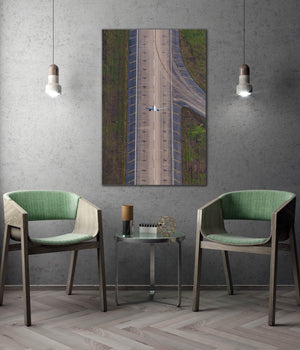 a modern living room with a large wall-mounted artwork depicting an aerial view of a road and a plane. The room is furnished with two green chairs, and there is a small table between them. The overall design and decor create a contemporary and stylish atmosphere.
